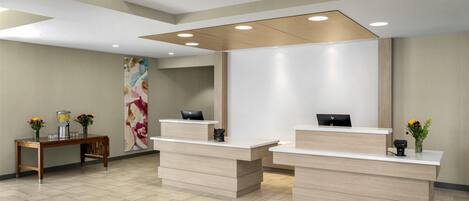 A reception area with two reception desks, a wooden side table with flowers, and a large abstract painting on the wall.