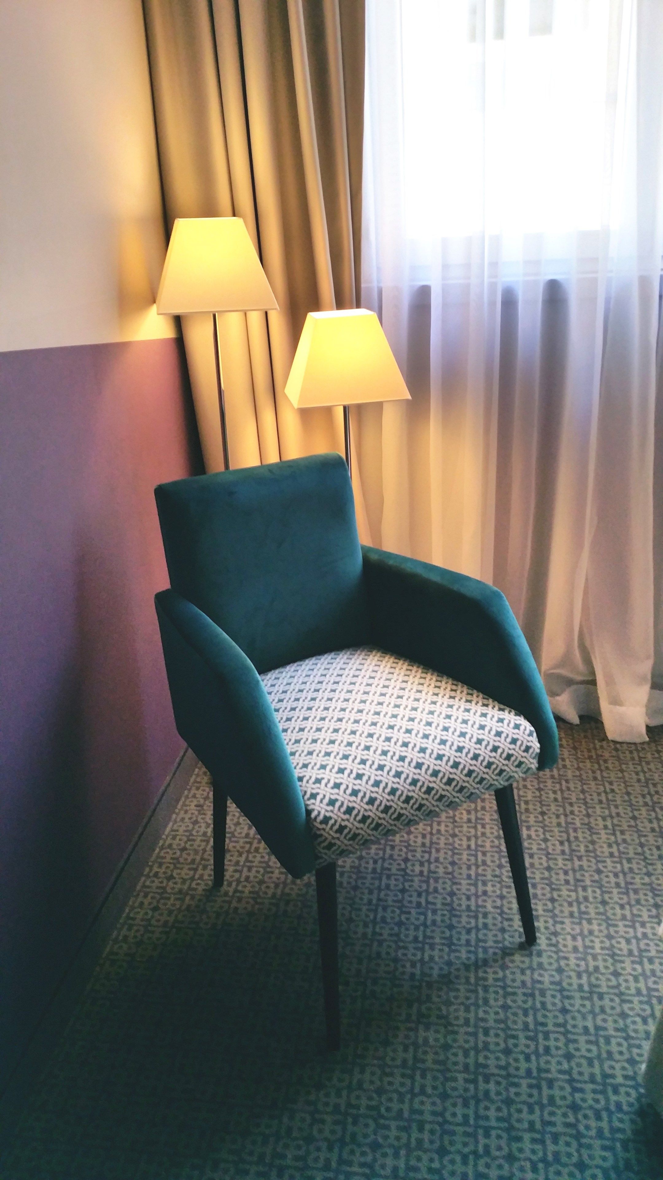 Un sillón color turquesa con un cojín estampado en una habitación de hotel.