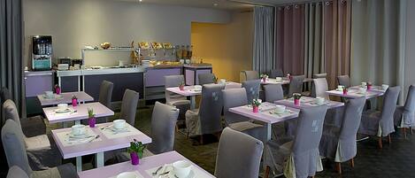 A modern dining area with multiple tables and chairs, a coffee machine, and a counter with food items.