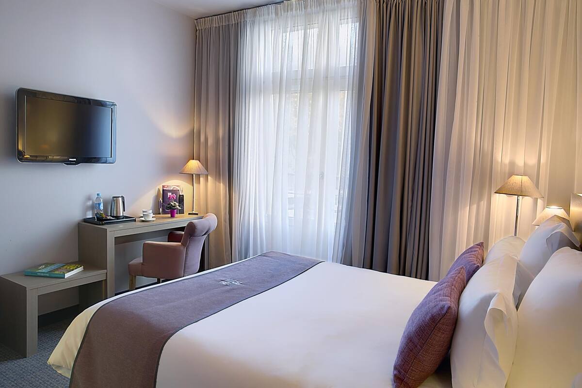 Ein Hotelzimmer mit Bett, Schreibtisch, Stuhl, Fernseher und Vorhängen.