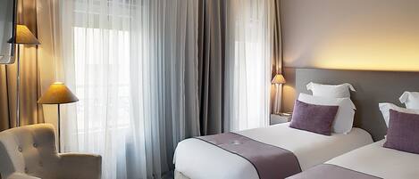 A hotel room with two beds, a chair, and a large window with sheer curtains.
