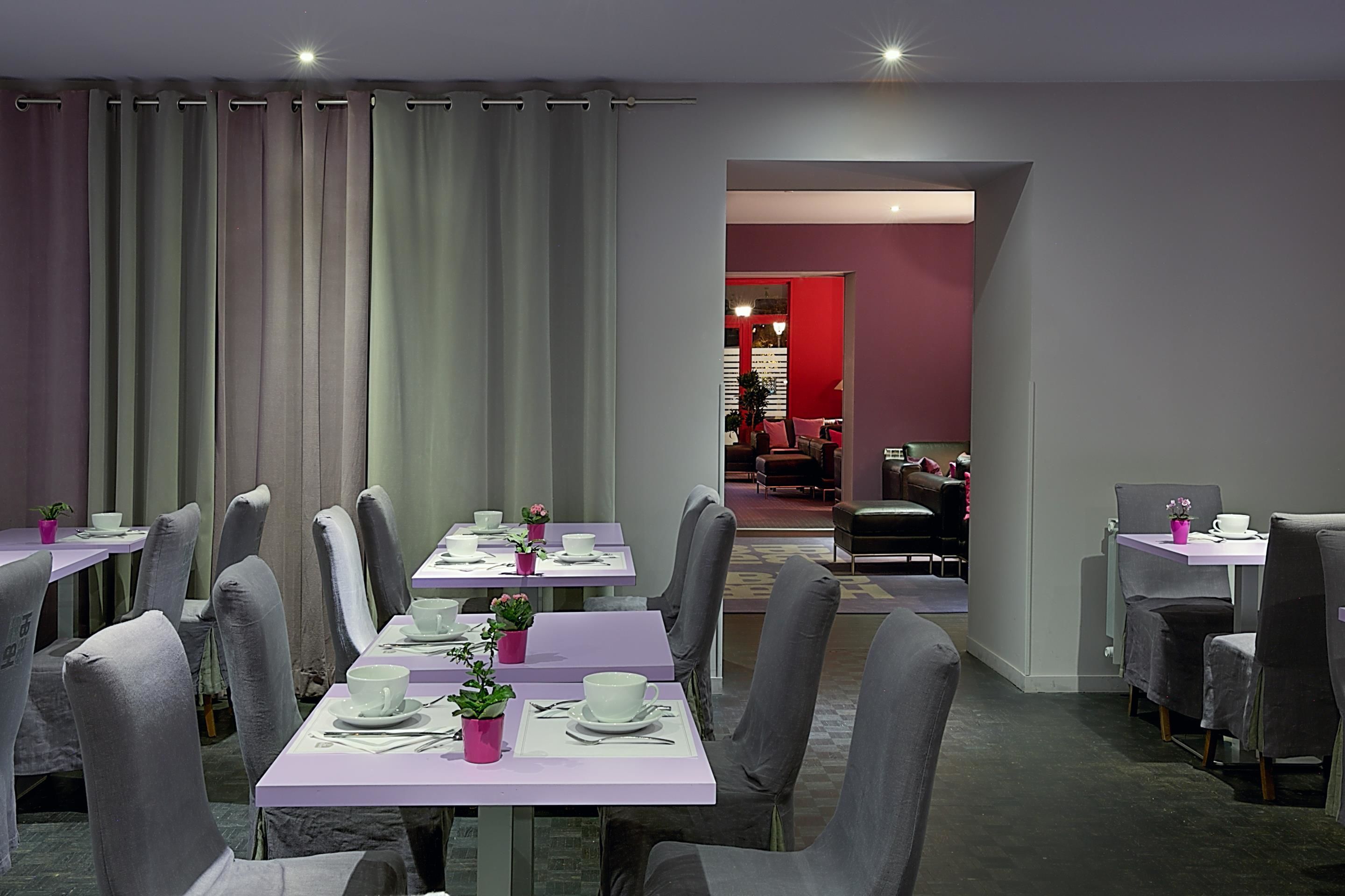 A dining area with multiple tables and chairs, a view into a room with red walls, and a ceiling light.
