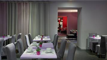 A dining area with multiple tables and chairs, a view into a room with red walls, and a ceiling light.