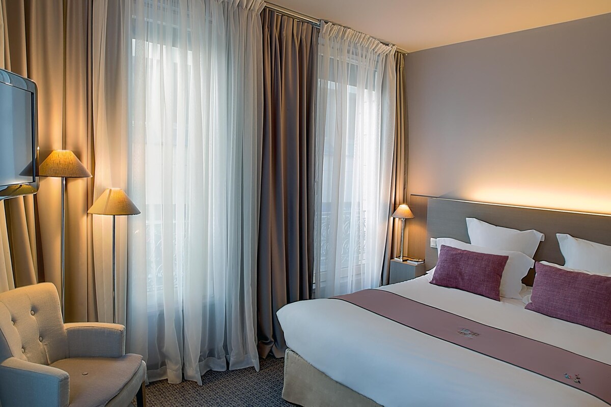 A hotel room with a bed, two bedside lamps, a chair, and a television.