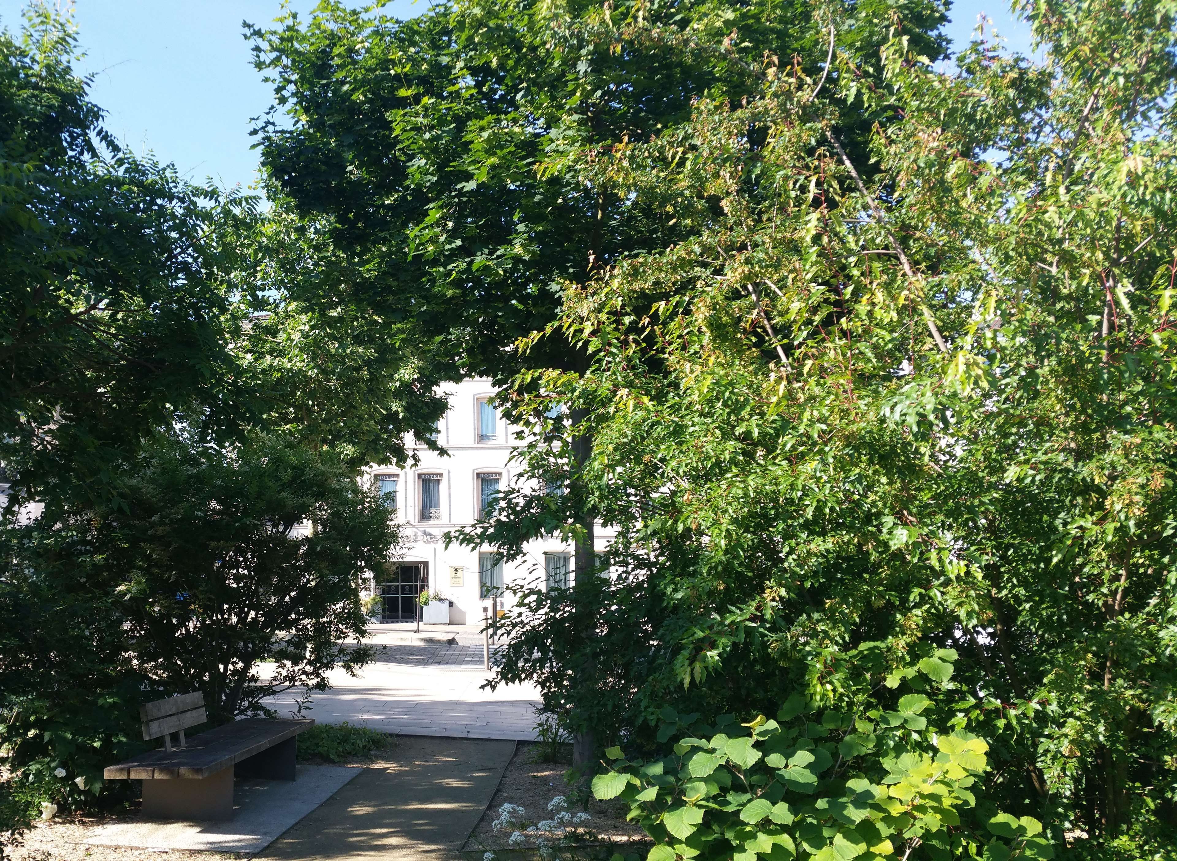A hotel with a central entrance, surrounded by lush greenery and a bench.