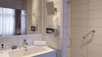A modern bathroom with a large mirror, a white sink, and a shower area.