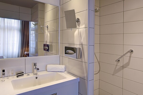 A modern bathroom with a large mirror, a white sink, and a shower area.