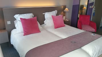 A hotel room with a large bed, two pillows, a nightstand, a lamp, and a red chair.