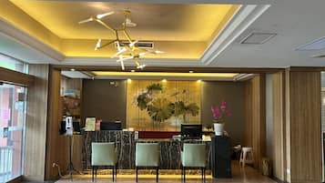 A reception area with a marble counter, two green chairs, a modern chandelier, and a large floral artwork on the wall.