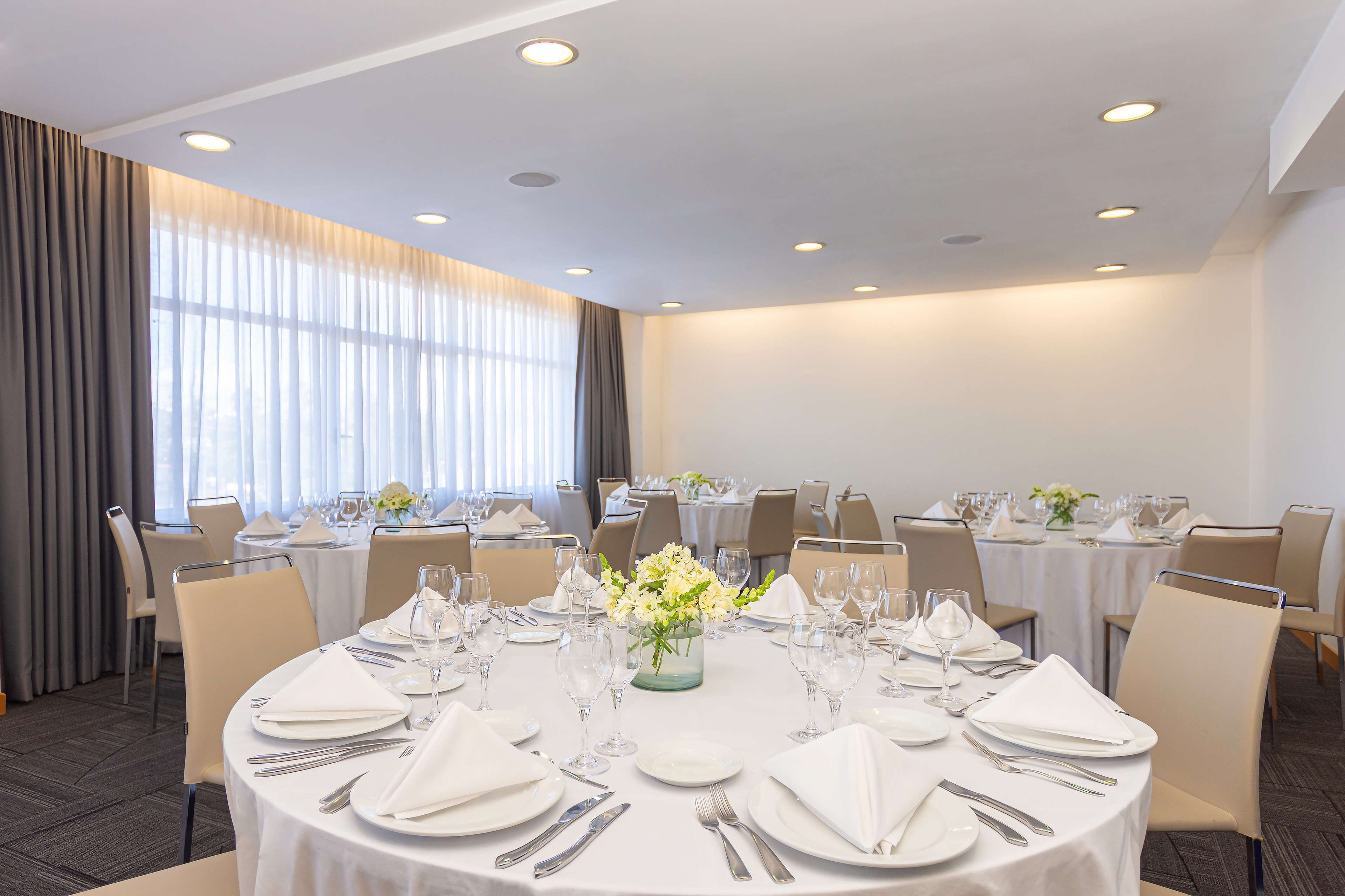 A conference room with round tables set for a formal event, equipped with nameplates, glassware, and floral centerpieces.