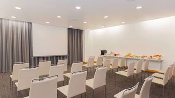 A conference room with rows of white chairs, a projector screen, and a buffet table with food.