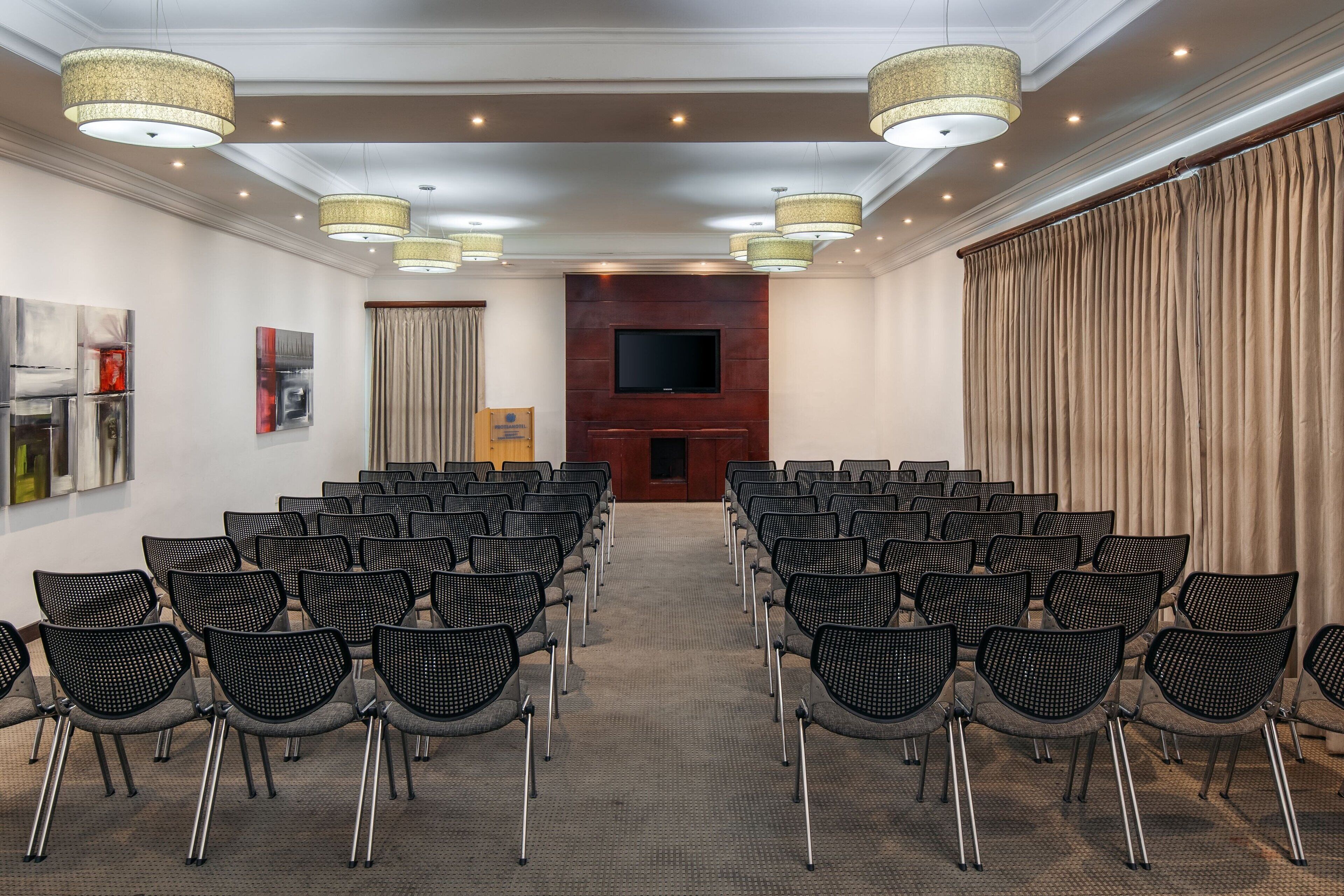 Un salón de conferencias con filas de sillas, una pantalla grande y lámparas decorativas.