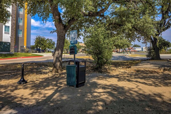 A pet waste station with a trash bin and a recycling bin, located in a shaded area with trees. - Motel 6 Cedar Park, TX (Cedar Park)