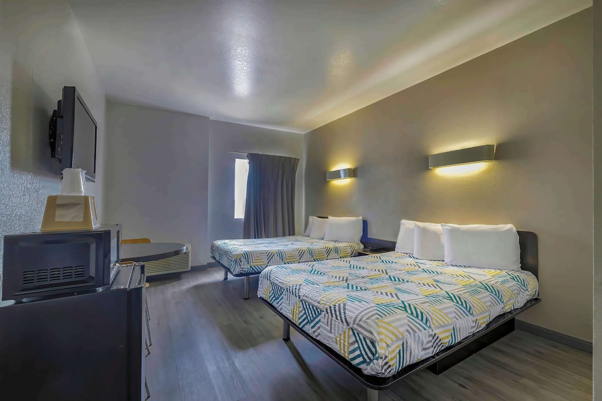 A hotel room with two beds, a TV, and a desk.