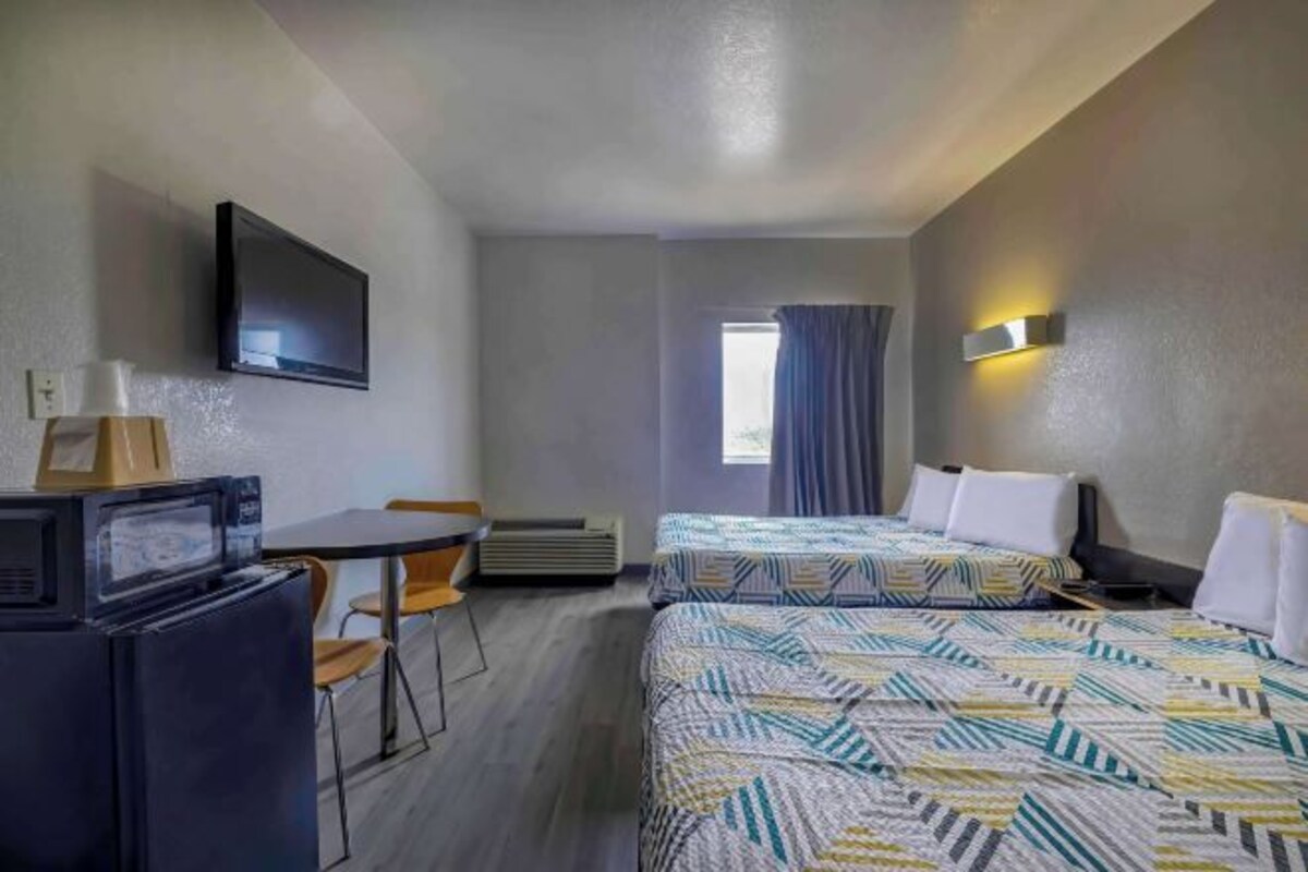 Quarto de hotel com duas camas, uma televisão, uma mesa de trabalho com cadeira e uma janela com cortinas.