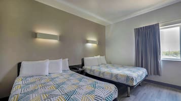 A hotel room with two beds, each with patterned bedding, a nightstand, a wall-mounted light, and a window with curtains.