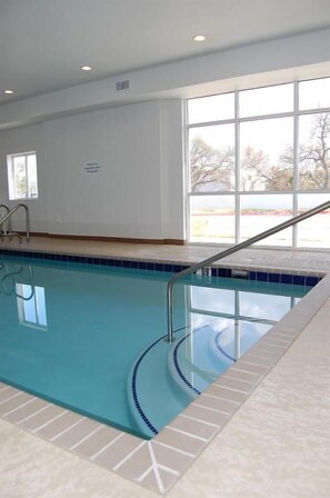 Piscina interior con agua azul cristalina, suelo de baldosas y una ventana que ofrece vistas al exterior.