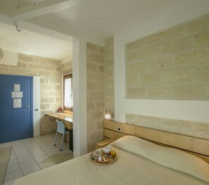 A room with a bed, a desk, and a chair. There is a tray with breakfast items on the bed. - Hotel delle Cave (Favignana)