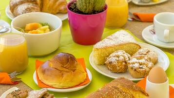 Una tavola imbandita con croissant, muffin, una ciotola di frutta e un bicchiere di succo d'arancia.