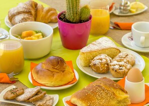 A breakfast table with croissants, muffins, a bowl of fruit, and a glass of orange juice. - Hotel delle Cave (Favignana)