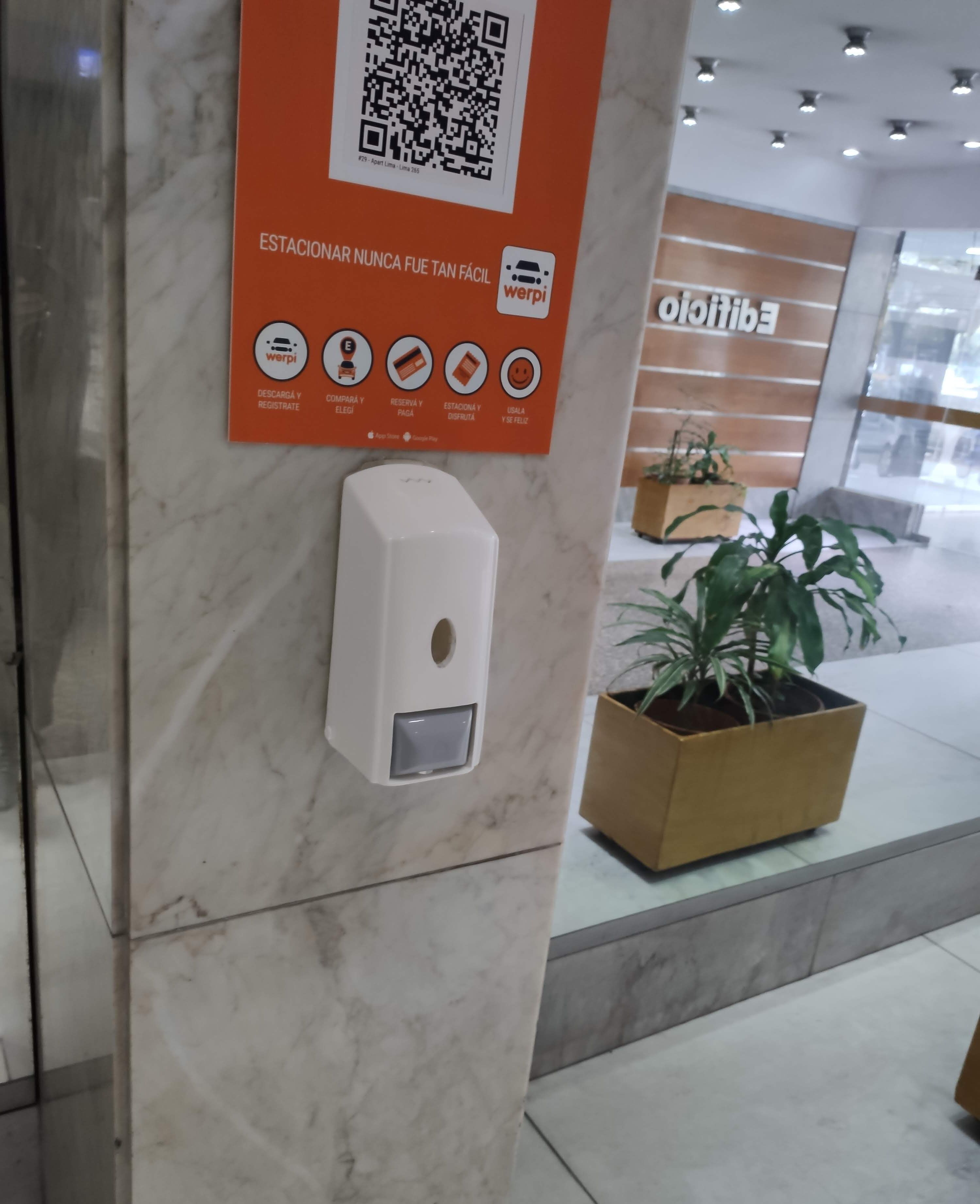 A QR code on a wall with a sign in Spanish, a digital payment station, and a potted plant.