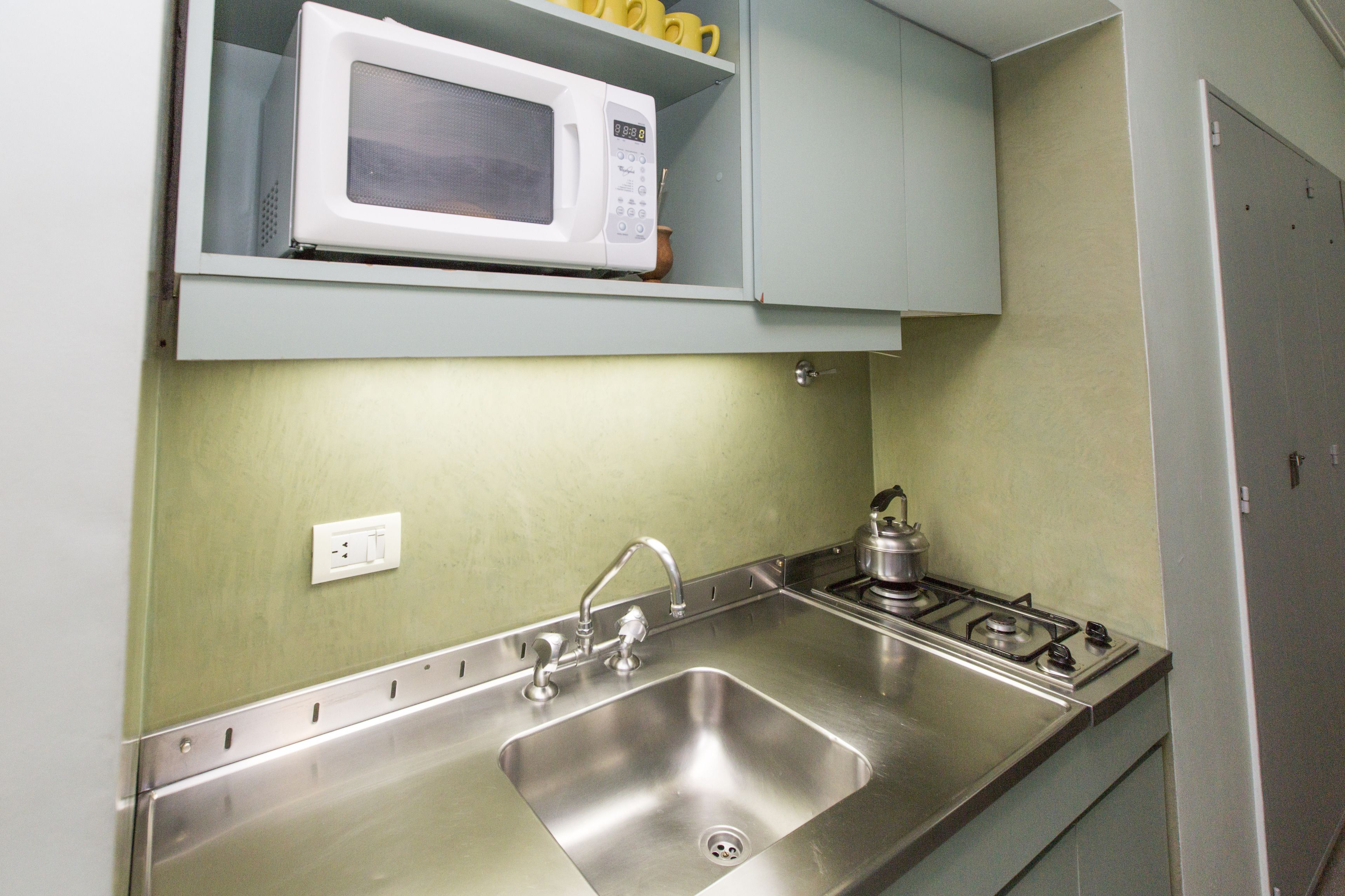 A kitchen with a stainless steel sink, a microwave on a shelf, and a stove.