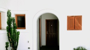A white building with a wooden door, potted plants, and a small window.