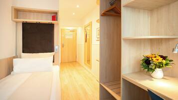 Una habitación de hotel con una cama, un armario de madera, un escritorio con lámpara y un jarrón de flores.