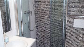 Et stilfuldt badeværelse med et brusebadekar i glas, en hvid vask og et toilet.