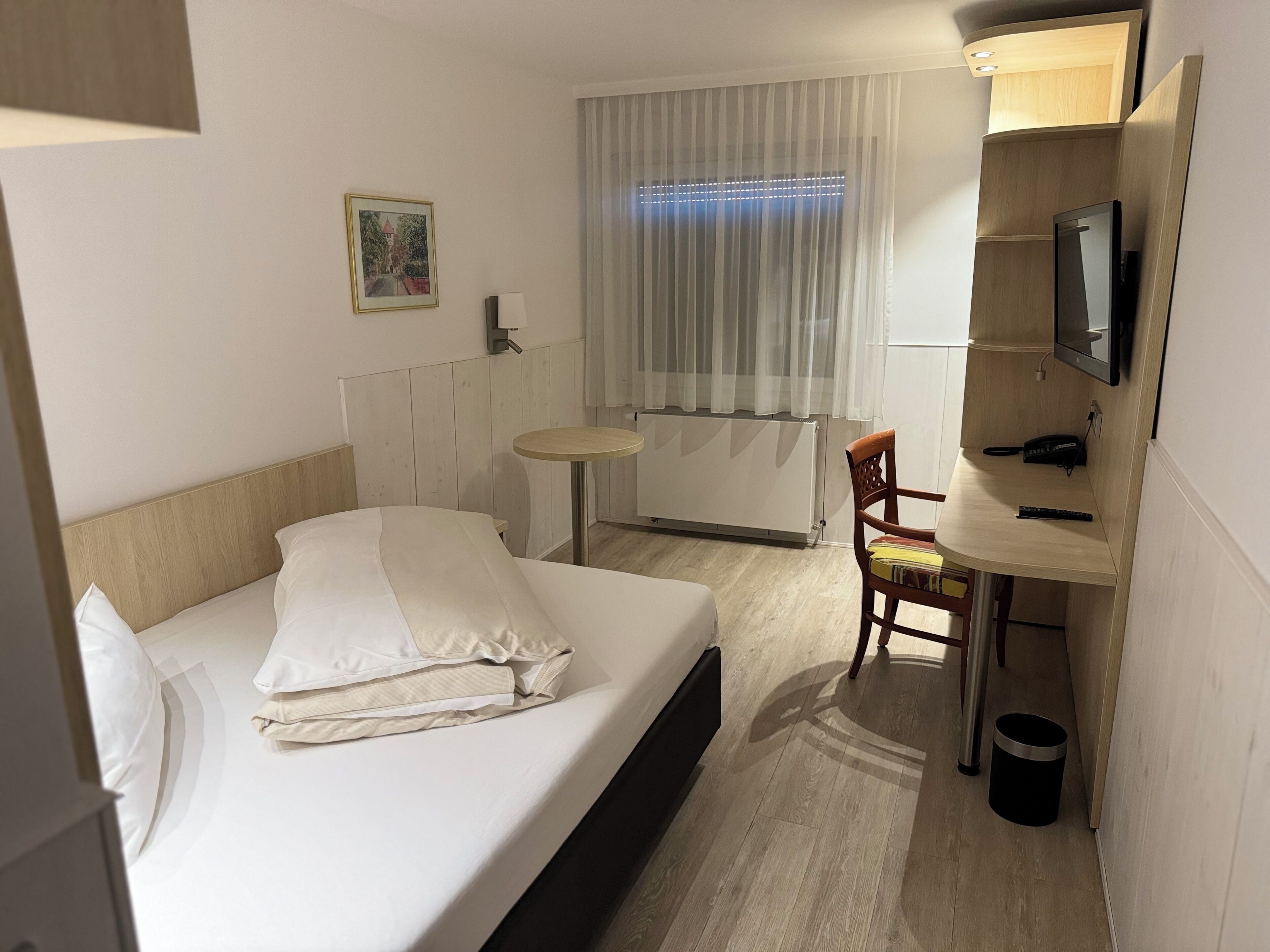 A hotel room with a bed, a desk with a chair, a television, and a window with curtains.