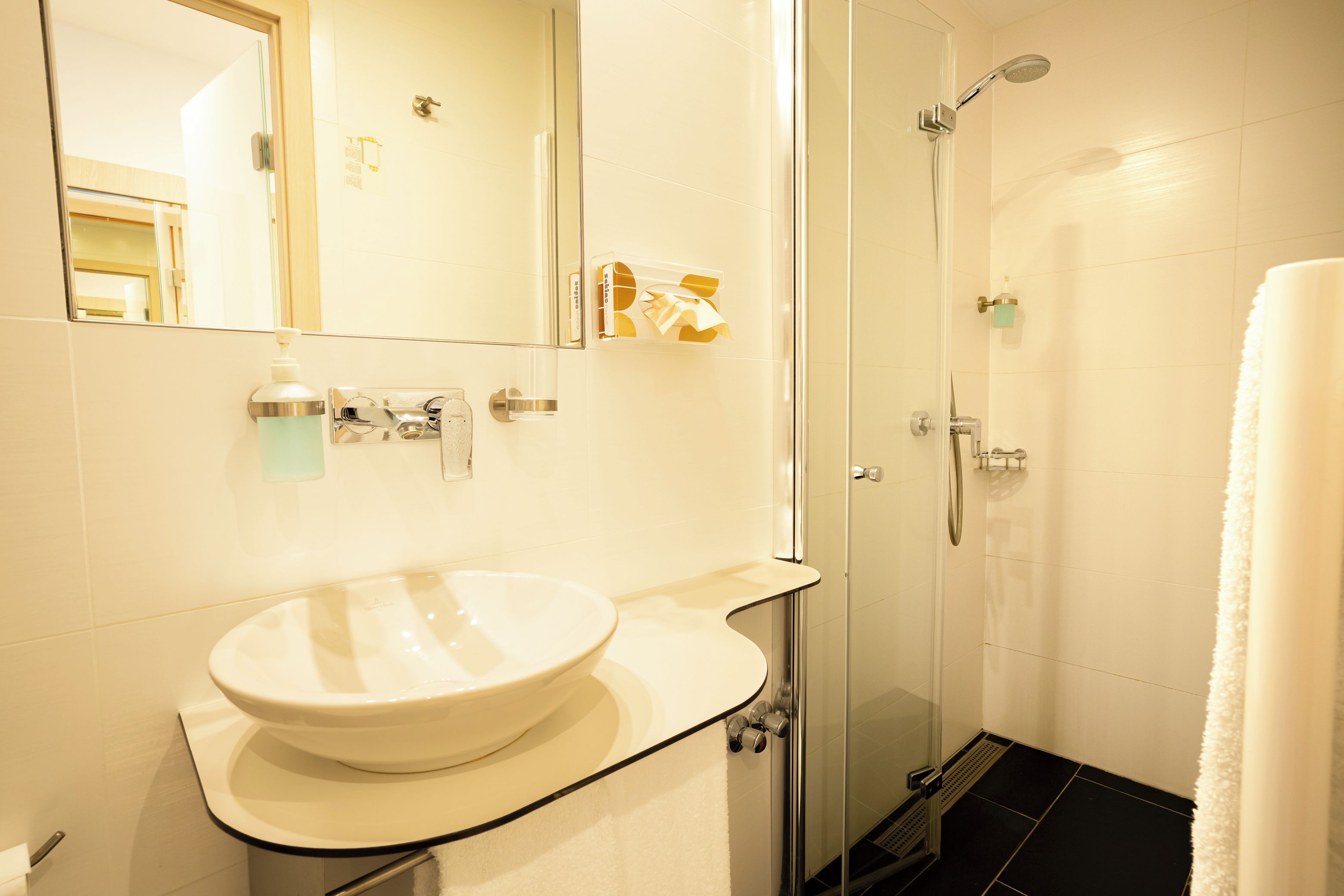 Un baño con lavamanos blanco, cabina de ducha con vidrio y un espejo.