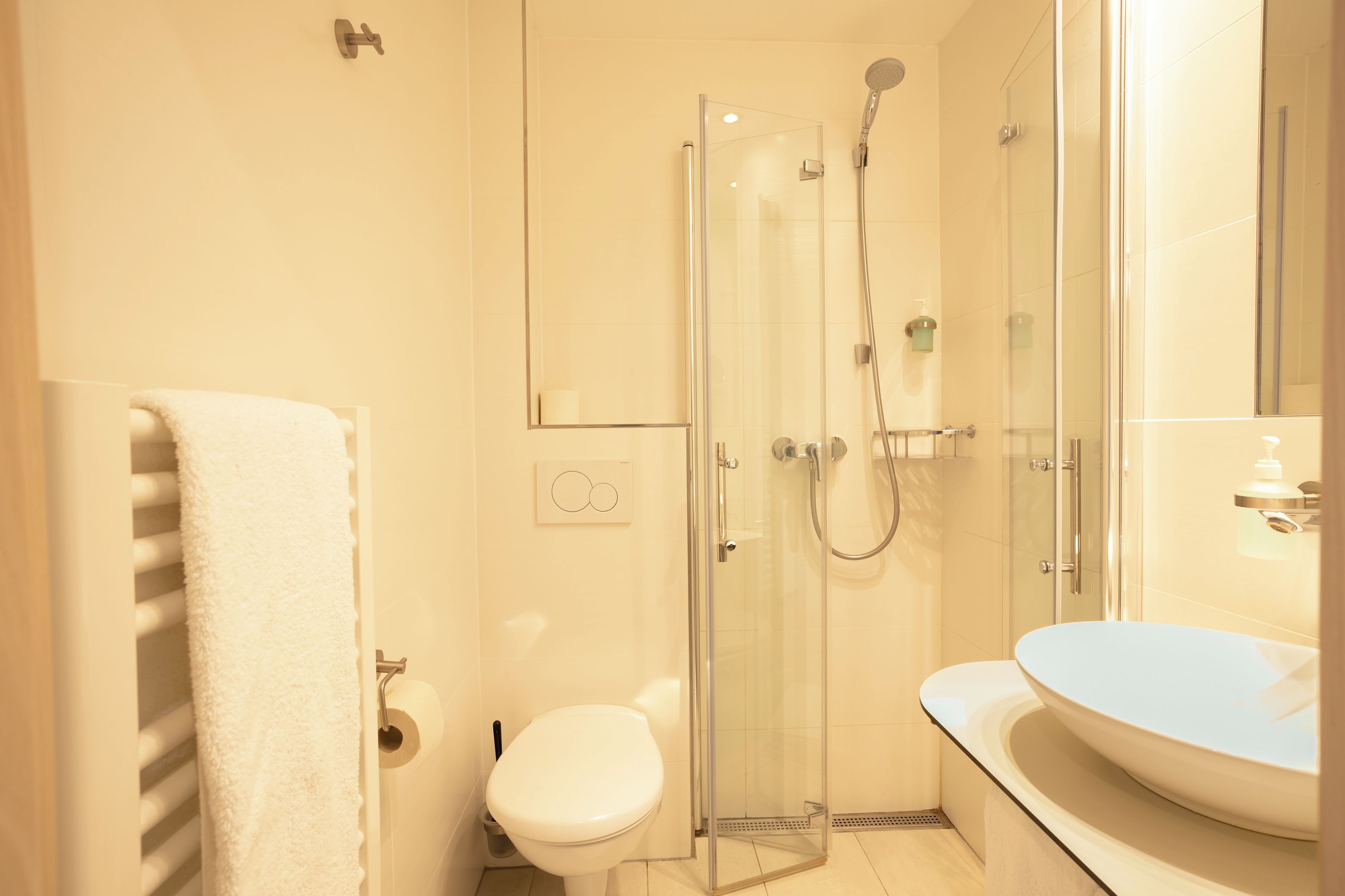 Un baño moderno con ducha de vidrio, inodoro blanco y lavabo redondo.