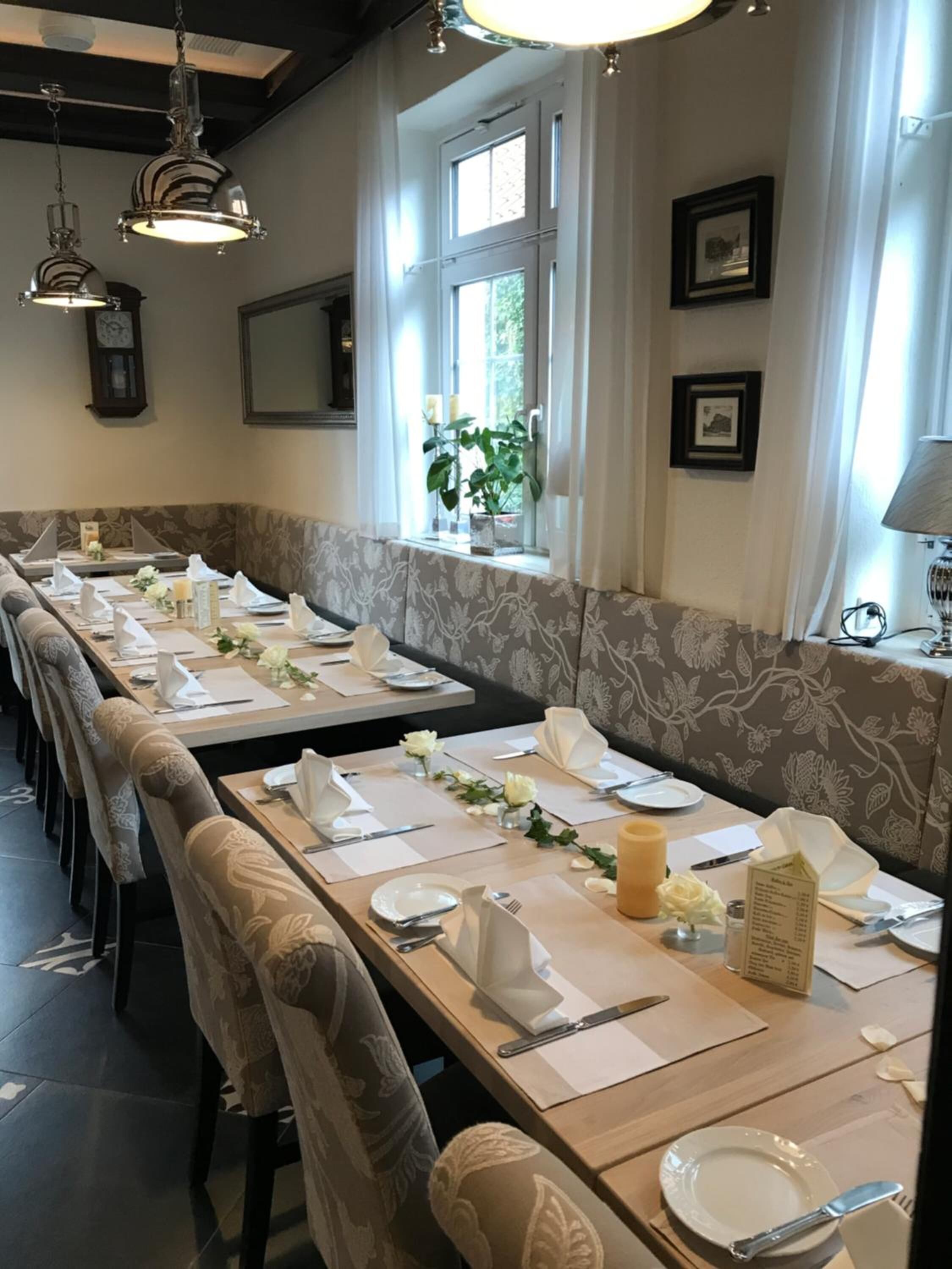 Een eetgedeelte met lange tafels gedekt voor bediening, een raam met een plant en een kroonluchter.