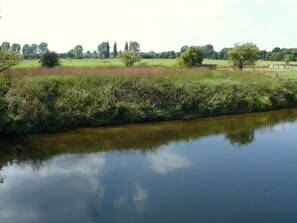 A calm river with a grassy bank and trees in the background. - Hotel Haase (Laatzen)