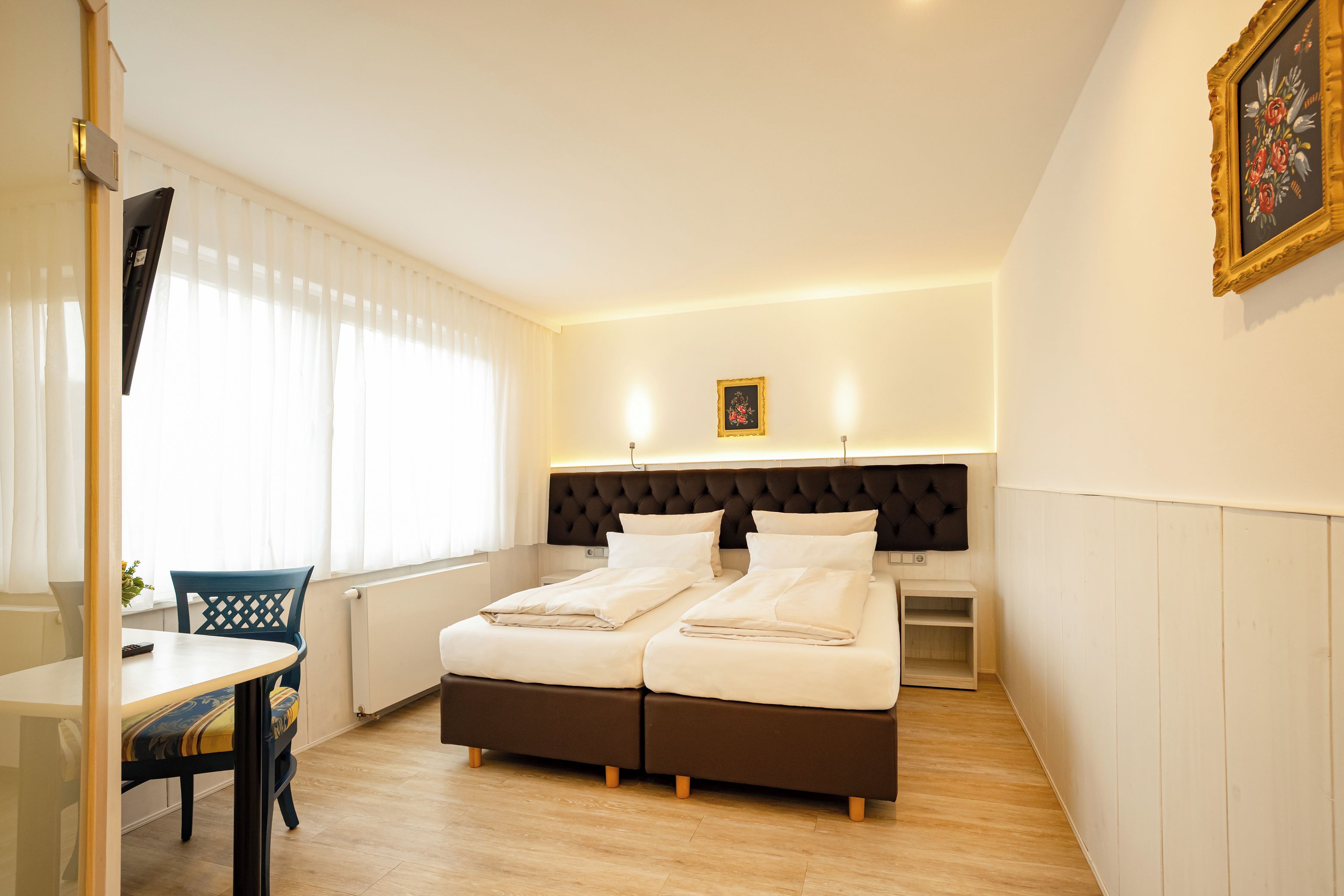 A hotel room with a double bed, bedside tables, a desk with a chair, and a window with curtains.