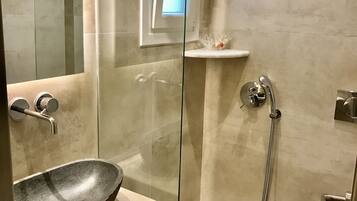 Um banheiro moderno com chuveiro de vidro, pia de pedra e um pequeno lavatório pedestal branco.