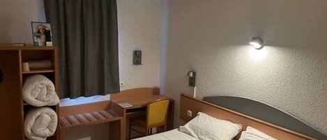 Een hotelkamer met een bed, een bureau, een stoel en een plank met handdoeken.