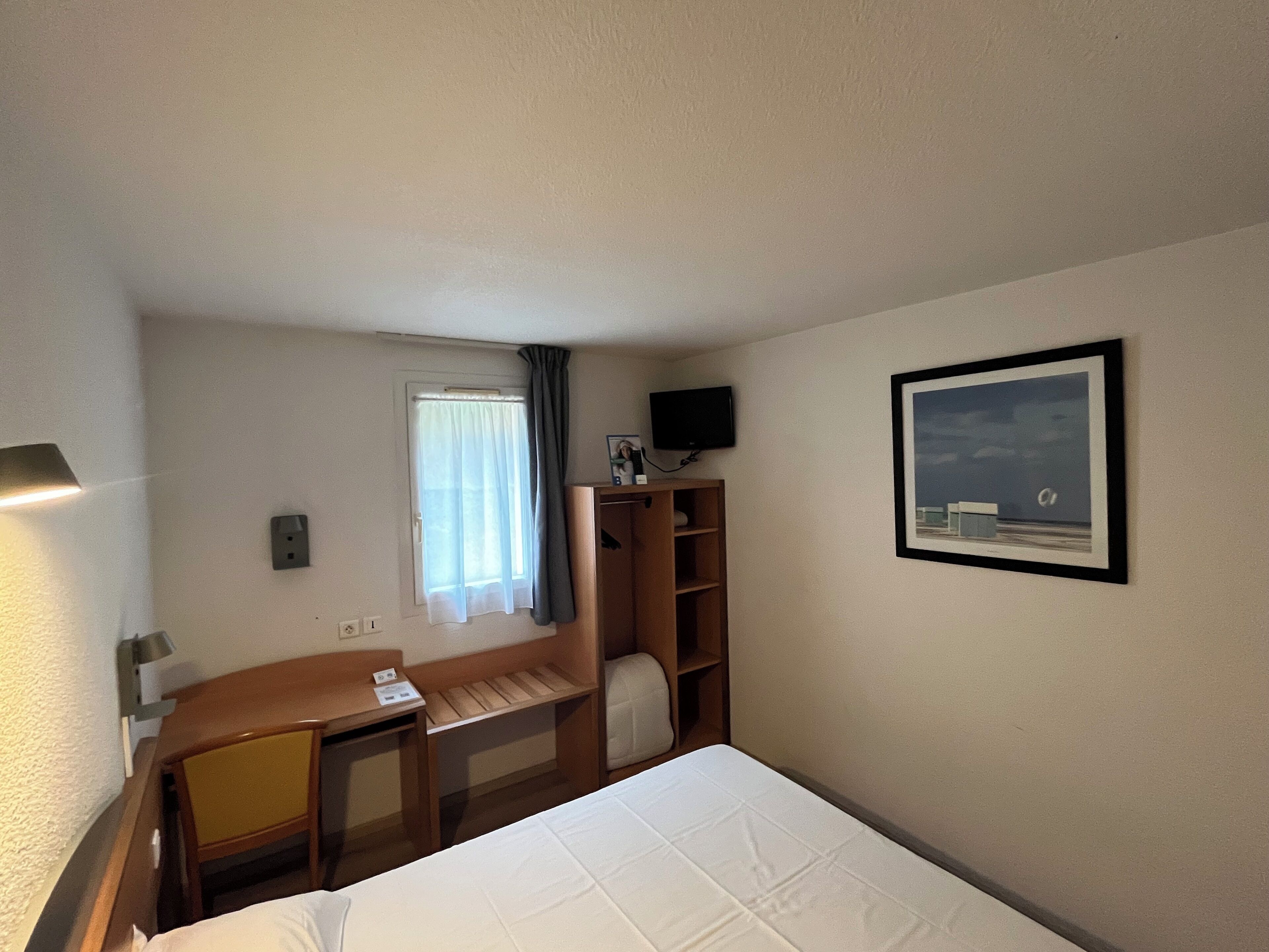 A hotel room with a bed, a desk, a chair, a television, and a picture on the wall.