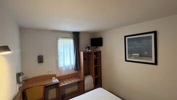 A hotel room with a bed, a desk, a chair, a television, and a picture on the wall.