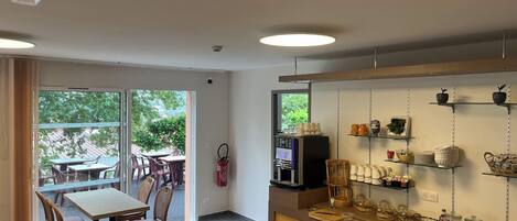 A modern kitchen with a coffee machine, shelves with kitchenware, and a dining area with chairs and a table.