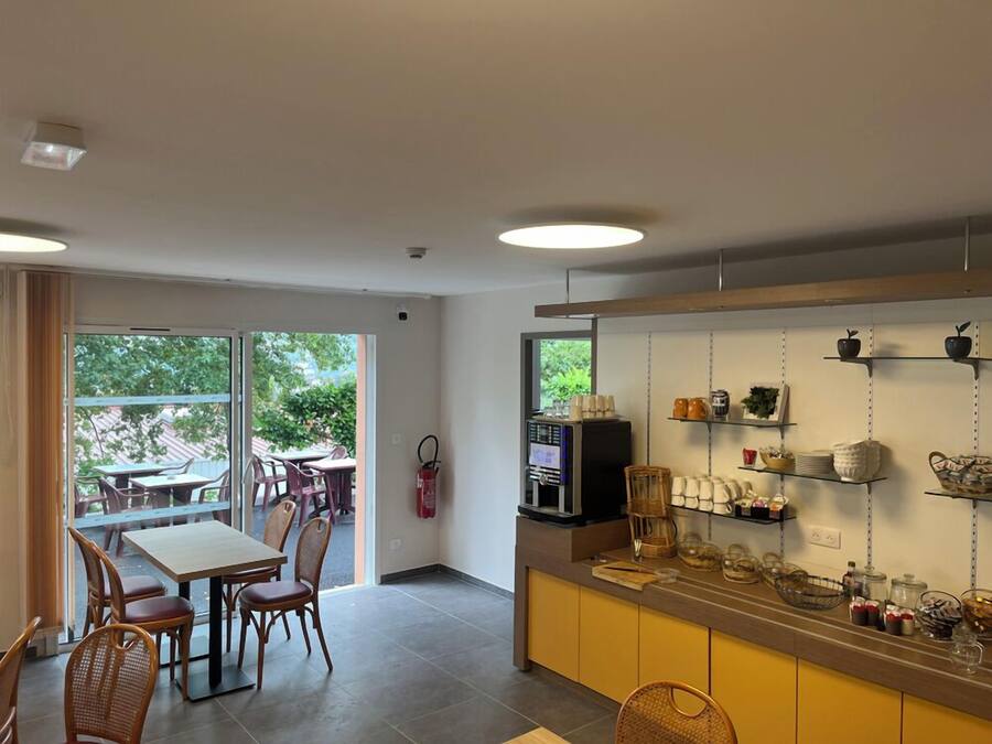 A modern kitchen with a coffee machine, shelves with kitchenware, and a dining area with chairs and a table.