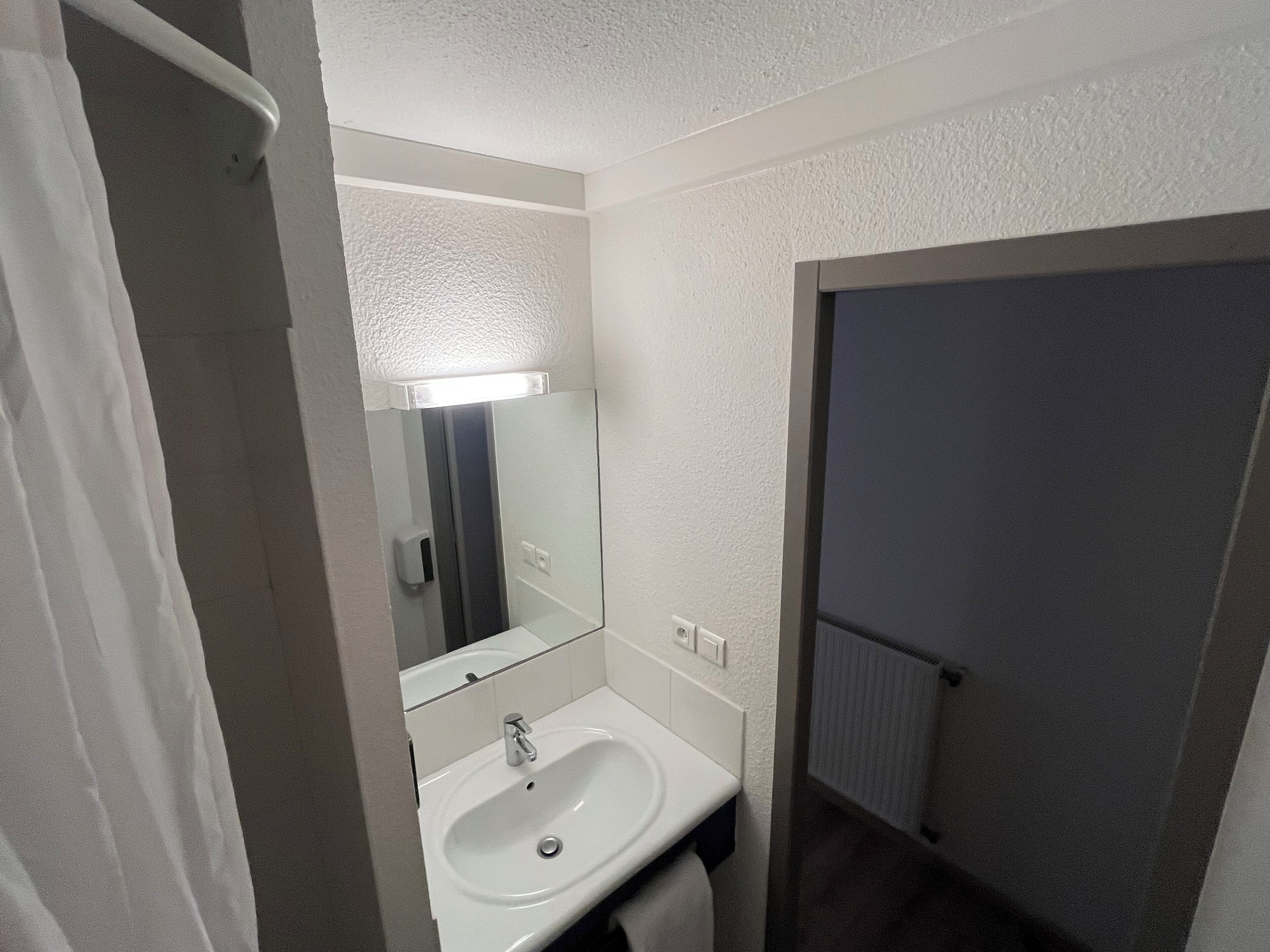 Une salle de bain avec un lavabo blanc, un miroir et un espace douche.