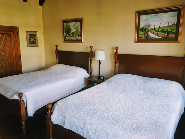 Two single beds with wooden headboards and white bedding in a room with two framed landscape paintings on the wall.