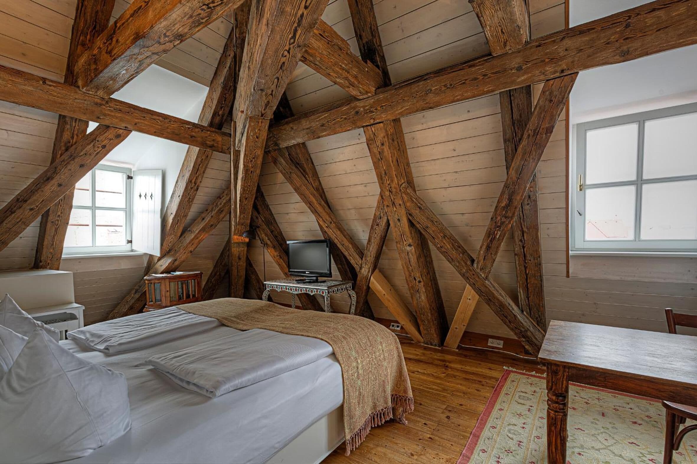 Une chambre avec un plafond en bois, un lit, une table et un téléviseur.