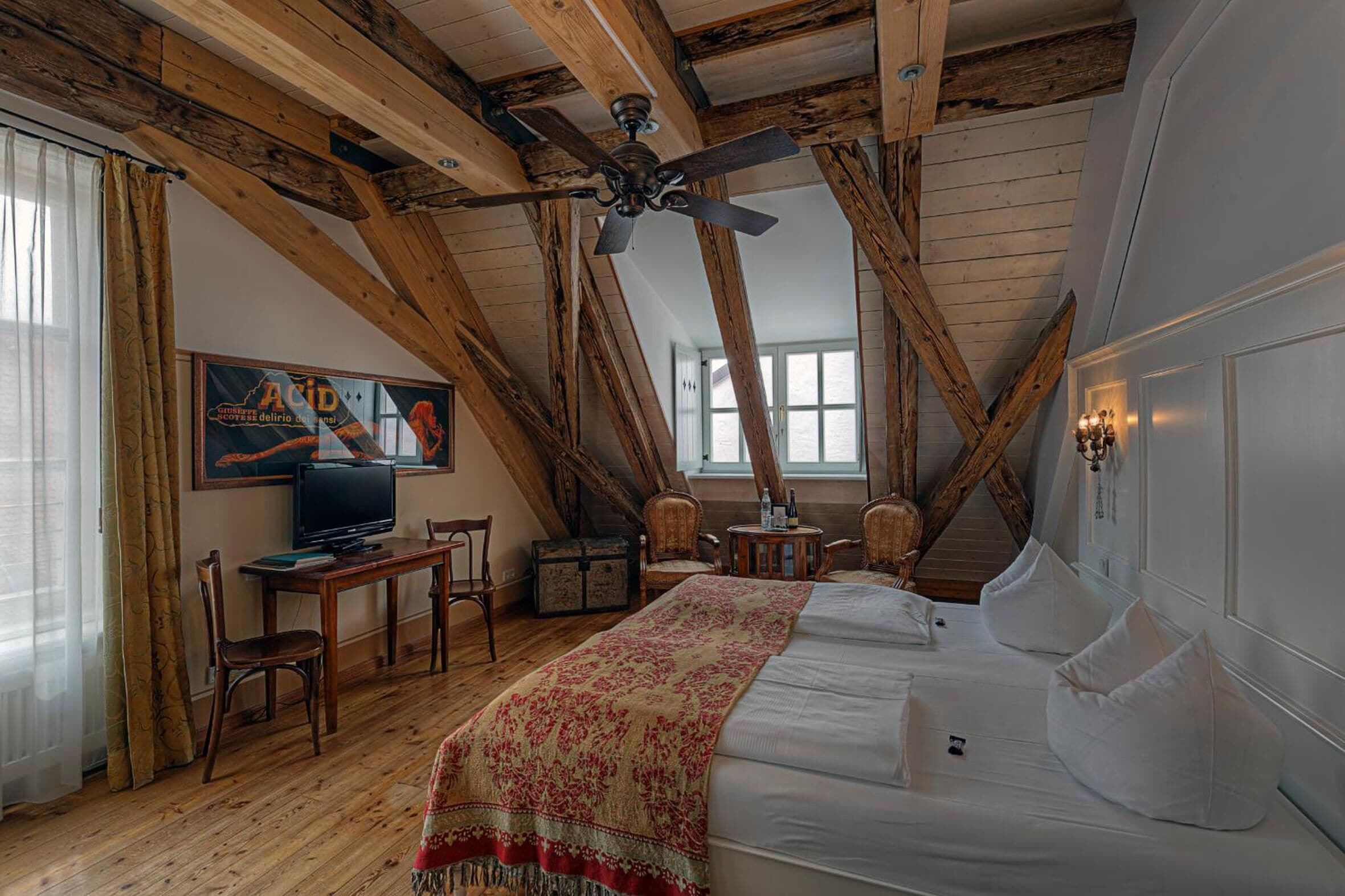 A bedroom with a wooden ceiling, a bed, a television, and a desk with chairs.