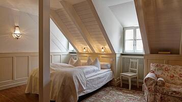 Een slaapkamer met een schuine kap, een bed met wit beddengoed, een stoel, een bloemenbank en een raam met daglicht.