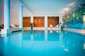 An indoor swimming pool with lounge chairs, wooden panels, and a mural of a mountainous landscape.