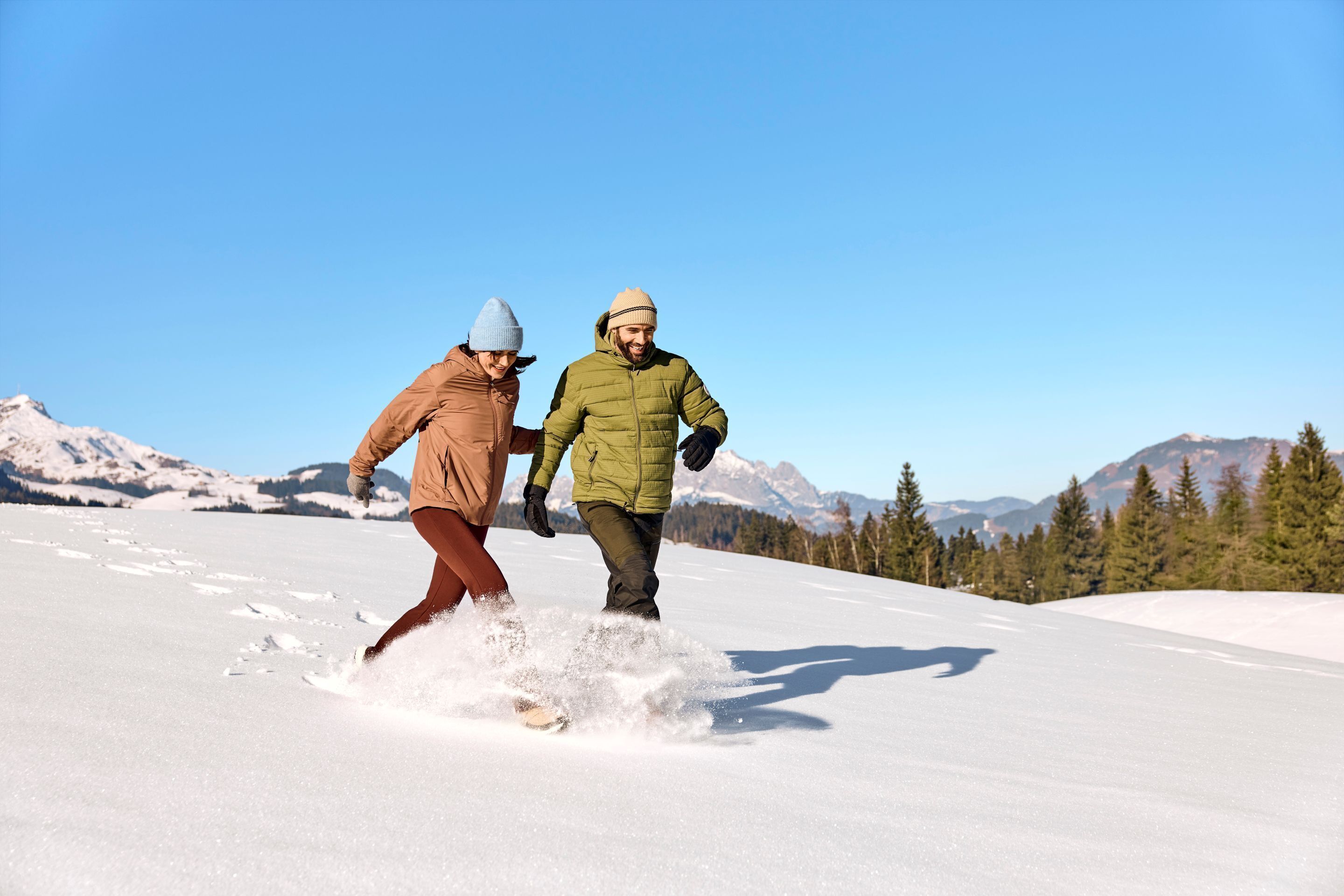 Deux personnes pratiquent la randonnée en raquettes par une journée ensoleillée, avec des montagnes en arrière-plan.