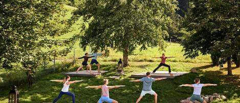 Un grupo de personas practica yoga al aire libre sobre plataformas de madera, rodeado de césped y árboles.