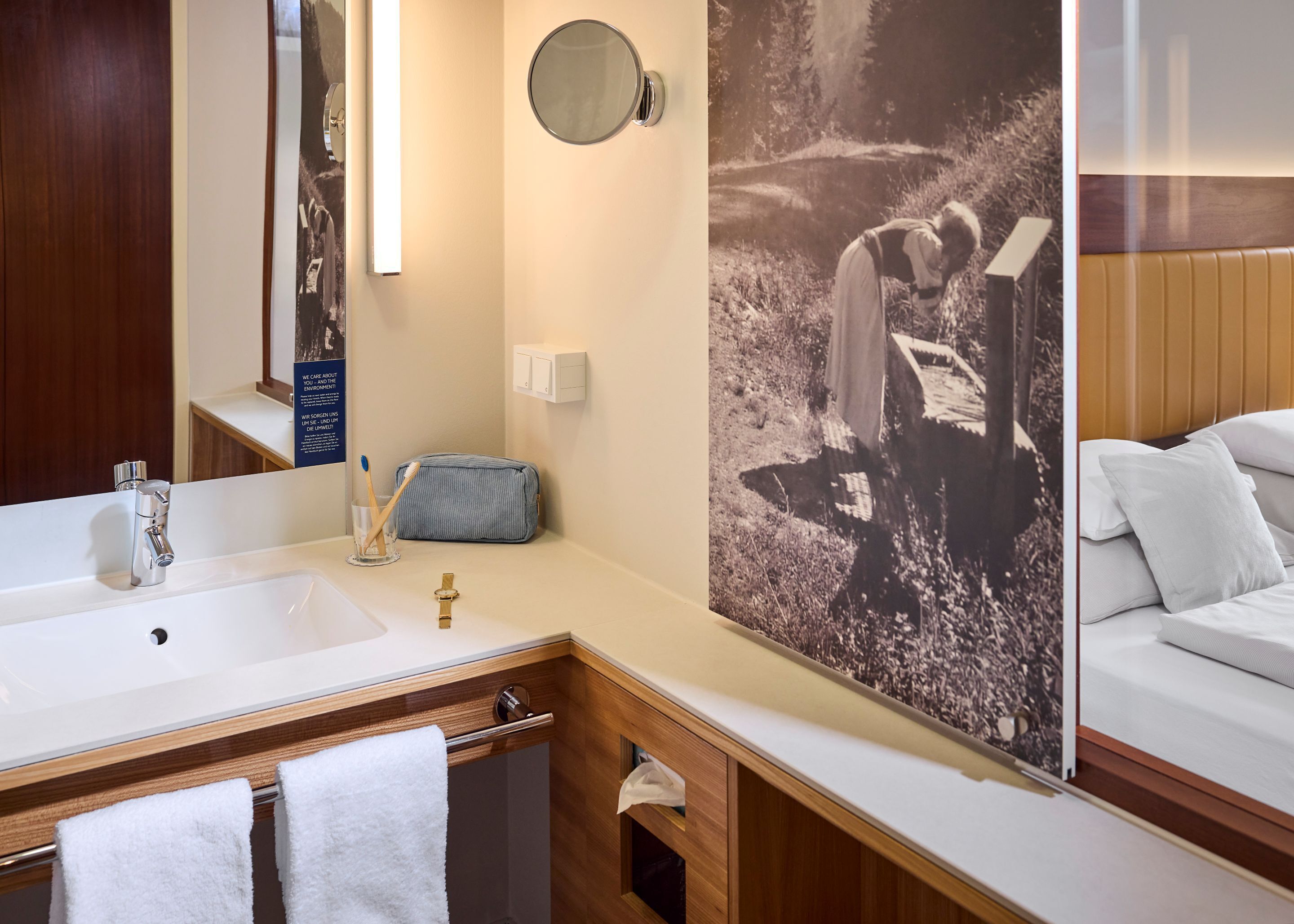 Ein Hotelbad mit Waschbecken, Spiegel, Handtuchhalter und Wandleuchte.